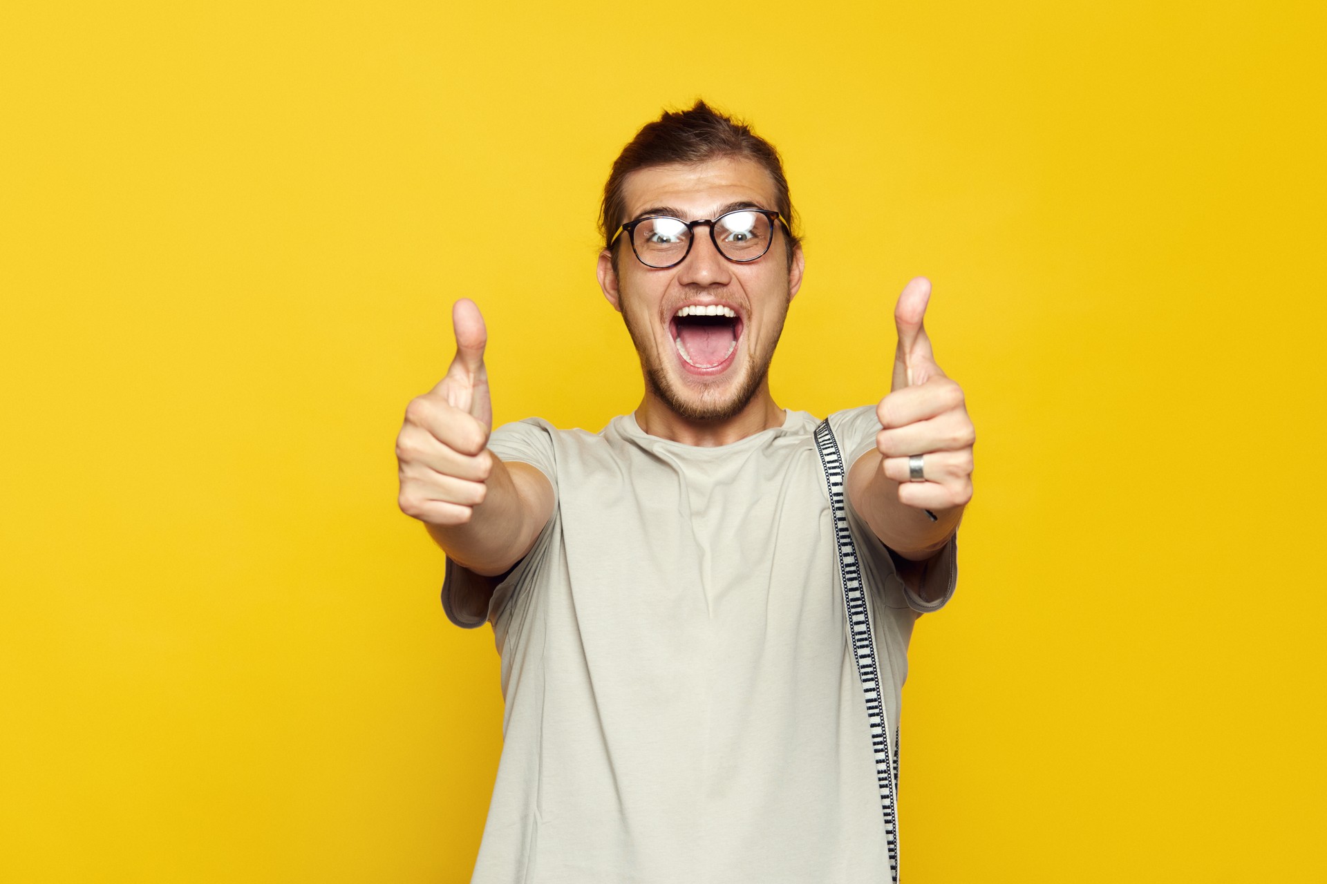 Attractive caucasian man smiling and showing thumb up gesture with both hands over yellow background and looking at camera.