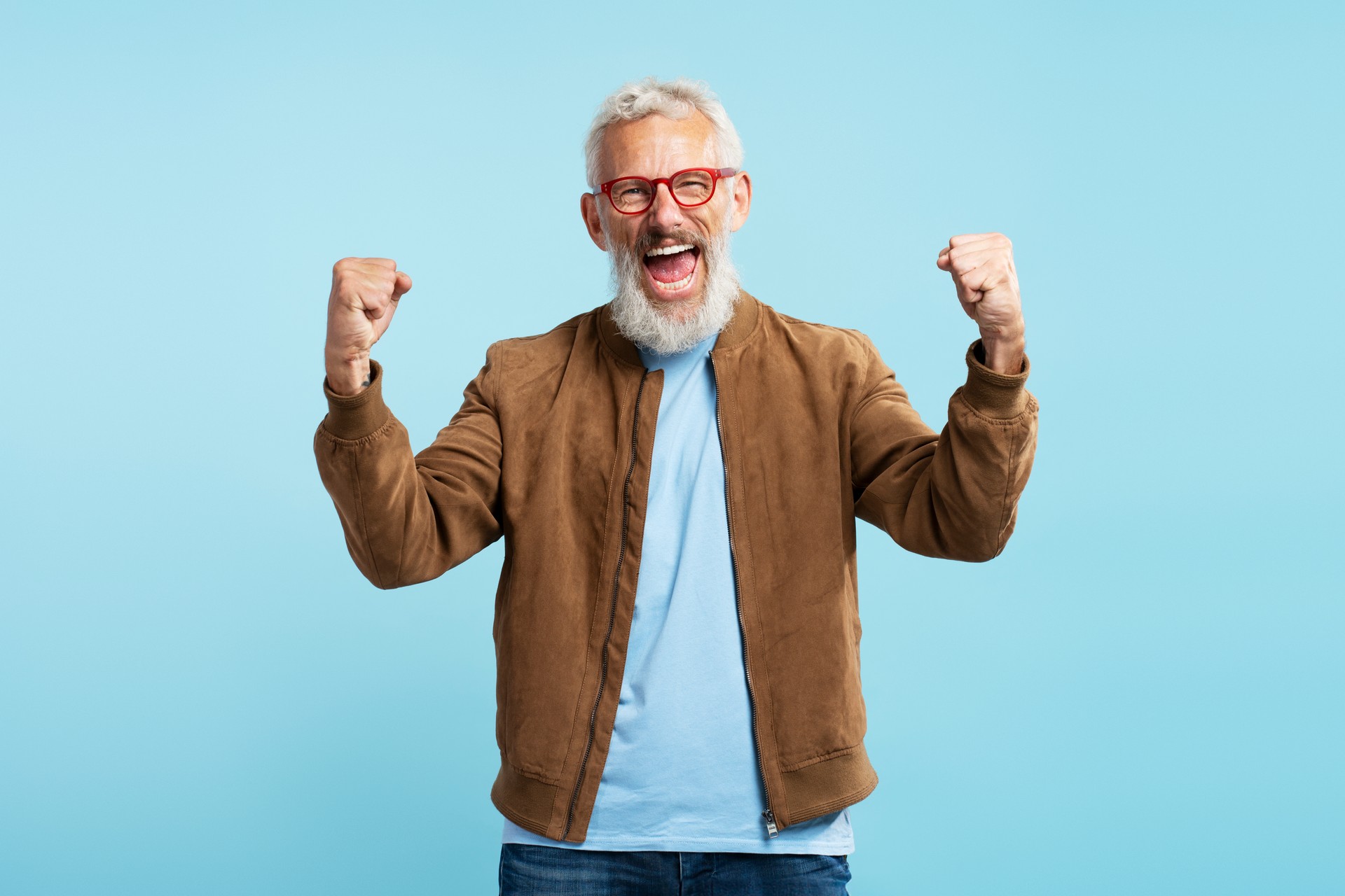 Excited mature man screaming, holding hands up, celebration success isolated on blue background